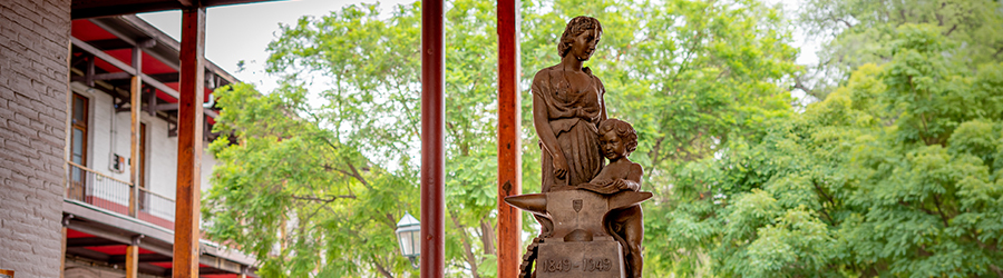 En la imagen aparece la escultura "Alma Mater", en la que se representa a una mujer con un niño al lado de sus piernas. Debajo de él y ella se encuentra escrito los años 1849 y 1949. Esta escultura se ubica en el pasillo central de la Escuela de Artes y Oficios.