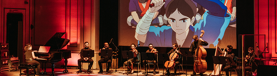 En la foto aparece una agrupación musical de jóvenes interpretando canciones populares del Studio Ghibli en el escenario del Aula Magna de la Usach.